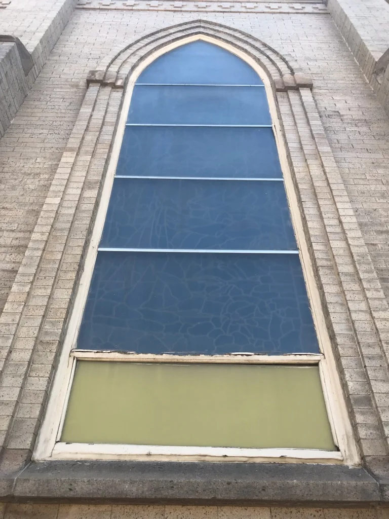 Arched window with blue glass panes and white trim on brick facade