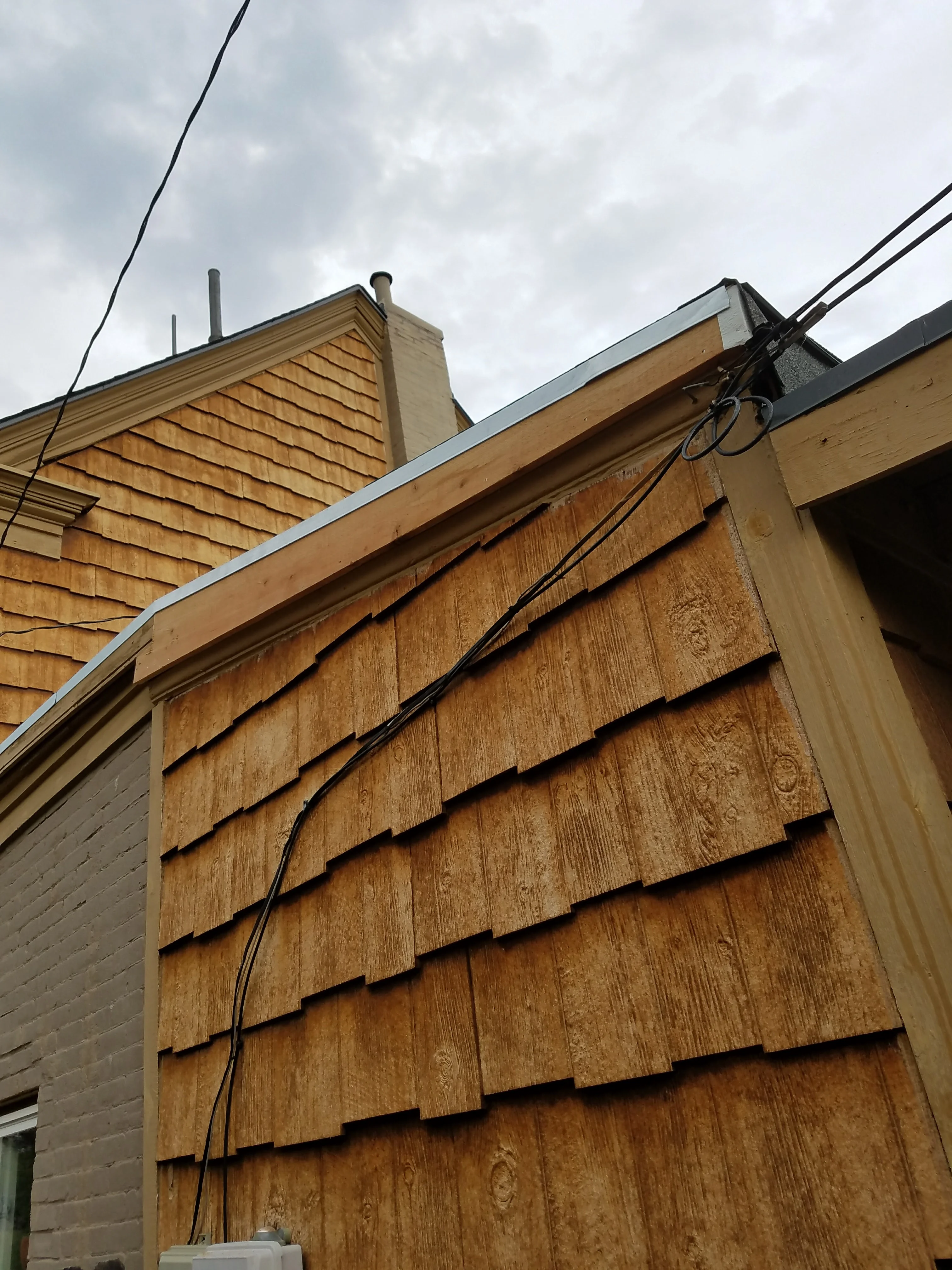 Newly installed wood shingle siding on home addition with metal roof trim and utility lines