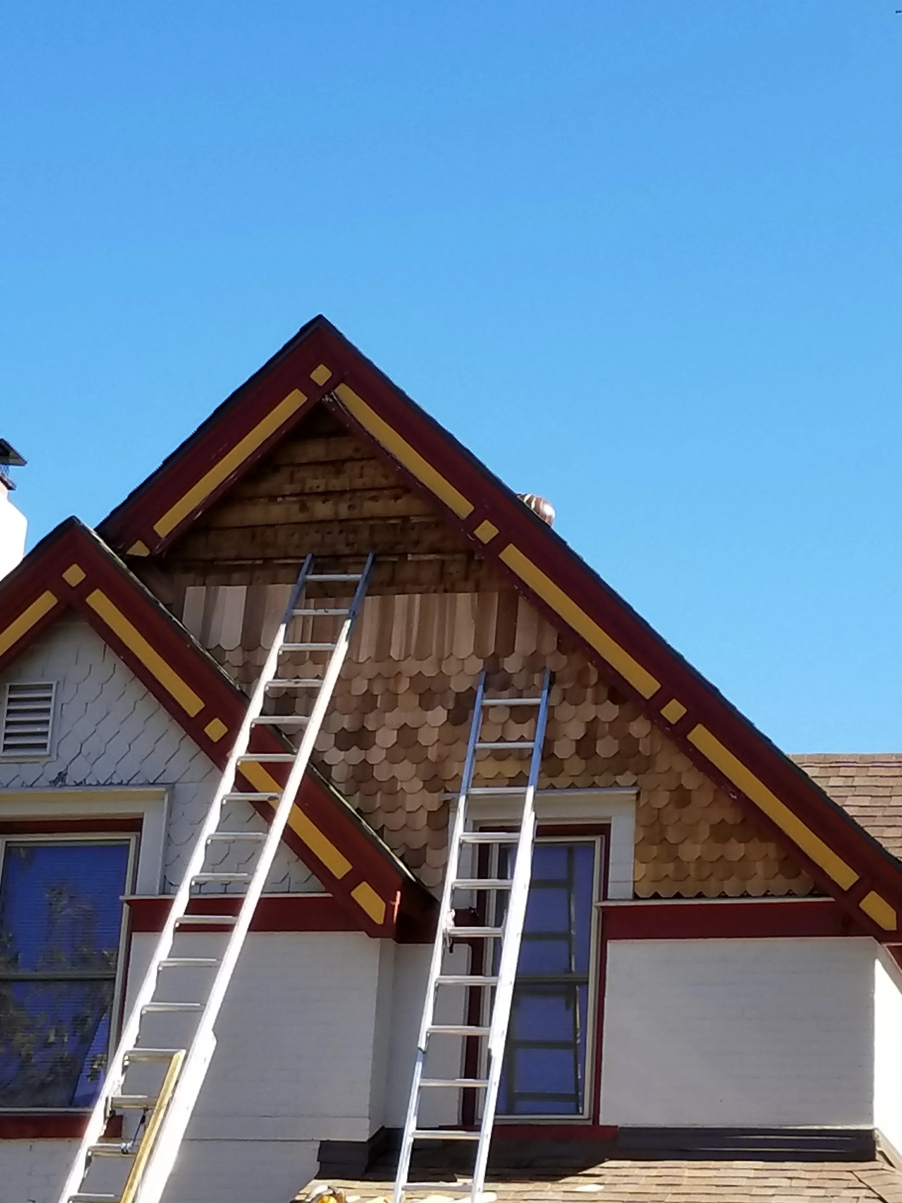 Residential gable with burgundy trim, gold accents, and wood shingles under clear sky