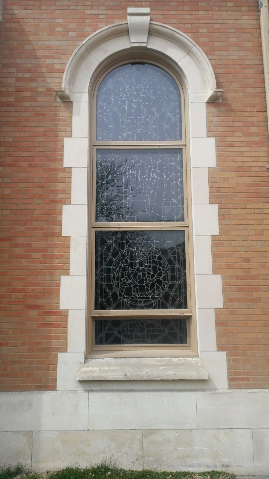Arched four-pane window with stone trim and keystones on red brick building