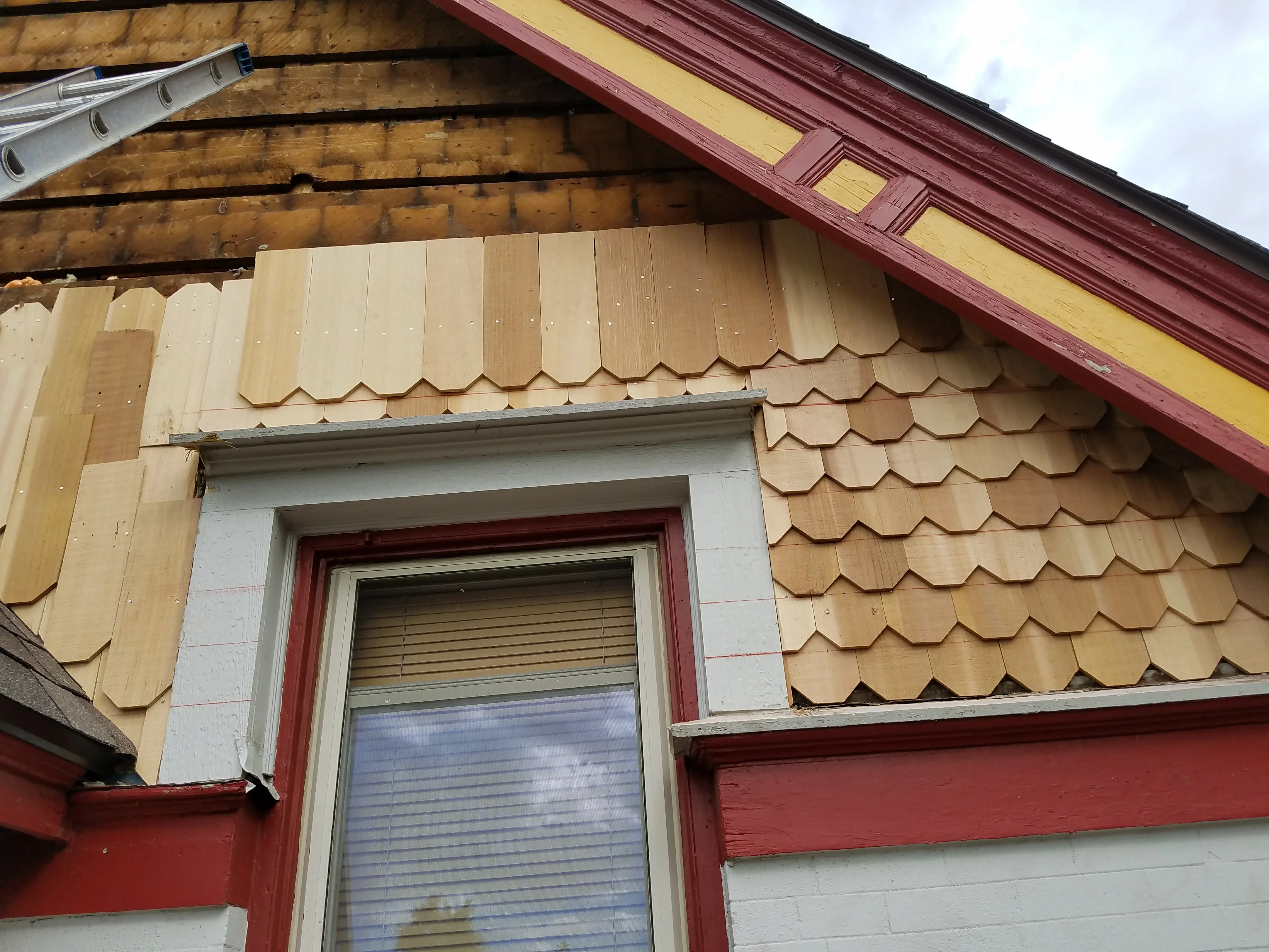 Wood shingle siding with scalloped edges installed around window opening with white trim and burgundy fascia