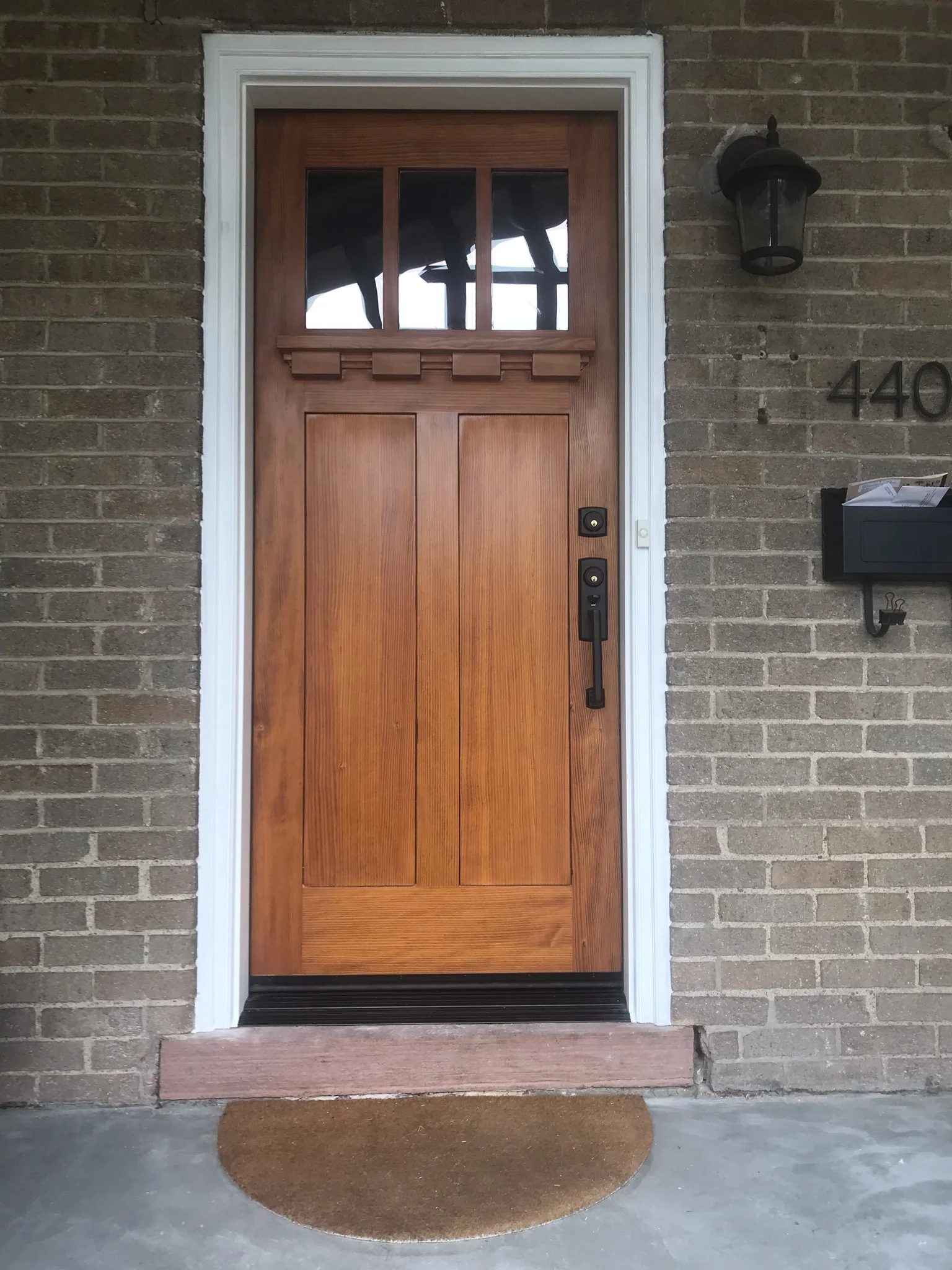 Wooden craftsman entry door with six-light transom and two-panel design on brick home