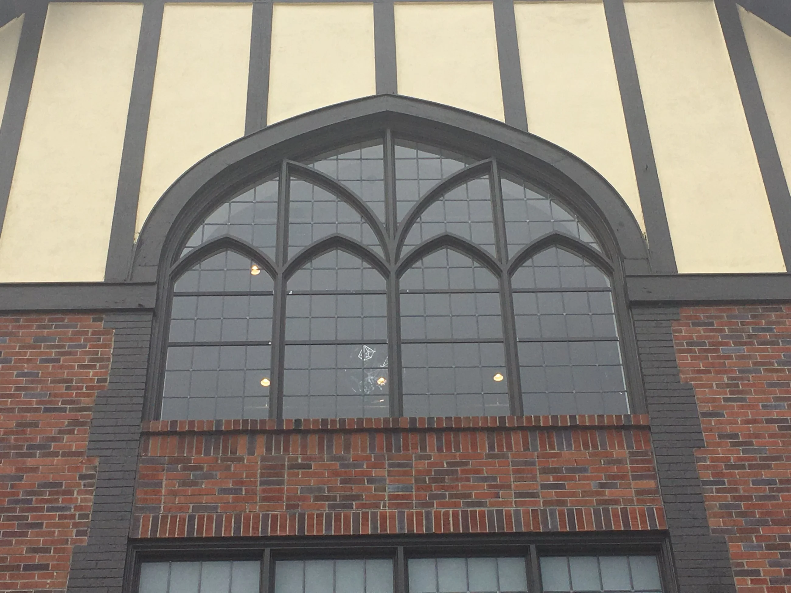 Large arched Gothic-style window with dark metal frame and grid muntins in brick building