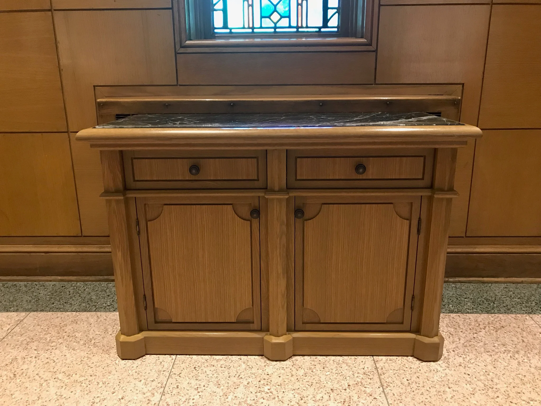 Custom wood vanity with marble top and decorative transom window in bathroom