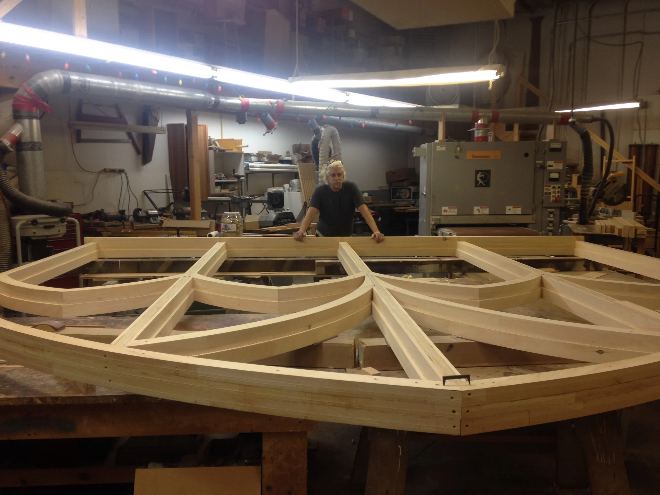 Craftsman standing behind large curved wood frame assembly in workshop