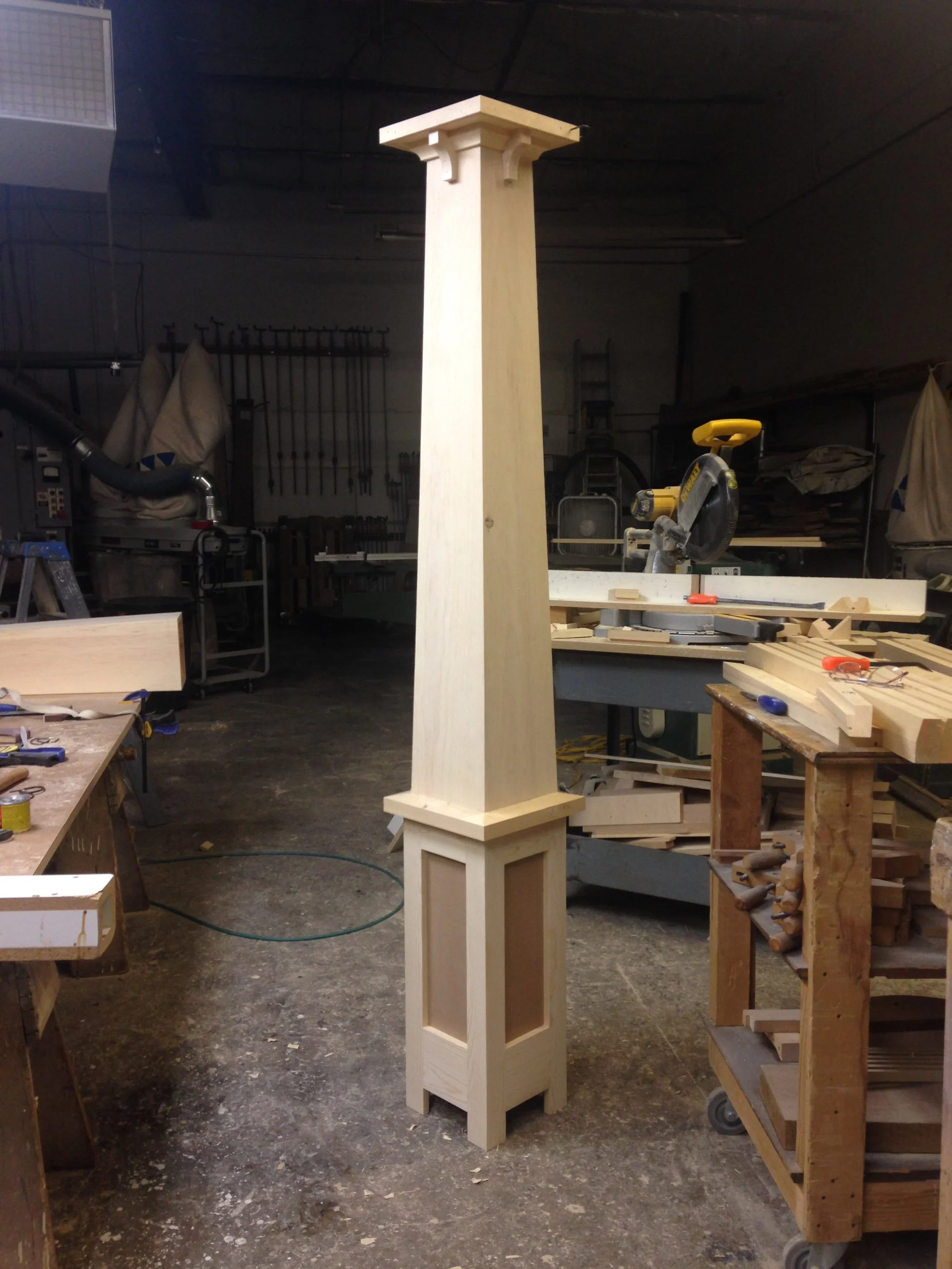 Tall wooden column with decorative corbels and paneled base in carpentry workshop
