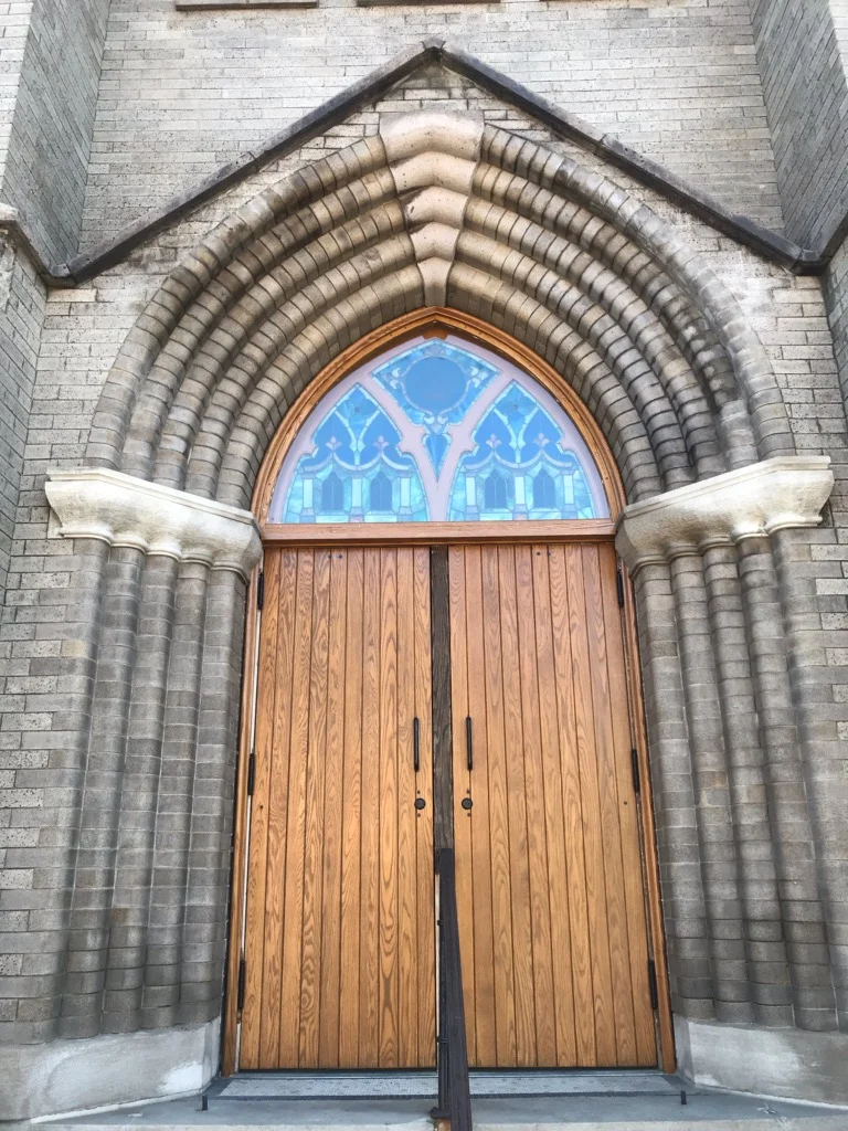 Gothic arched wooden double doors with blue stained glass transom window and stone molding